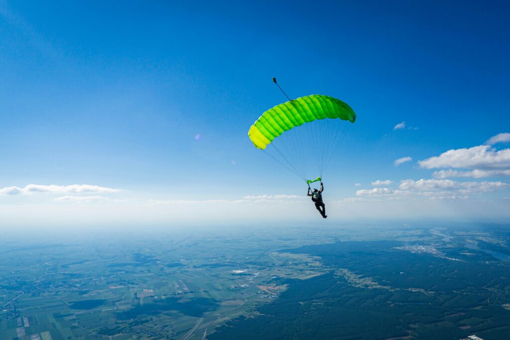 A skydiver under an open green canopy above the clouds